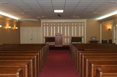 Interior of a church sanctuary with rows of wooden pews facing a central pulpit and red carpet aisle.