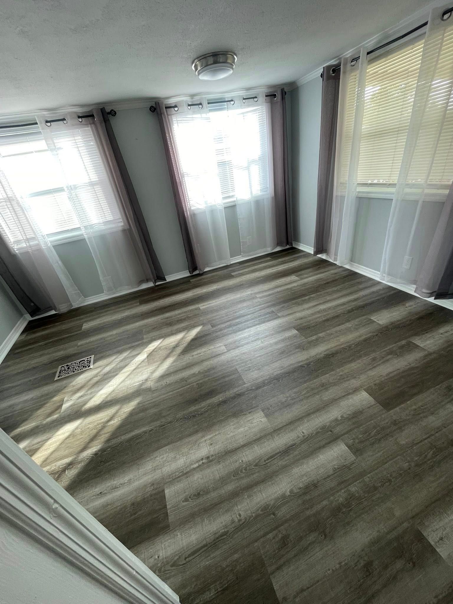 Empty room with gray wood-look flooring, pink walls, and large windows with blinds.