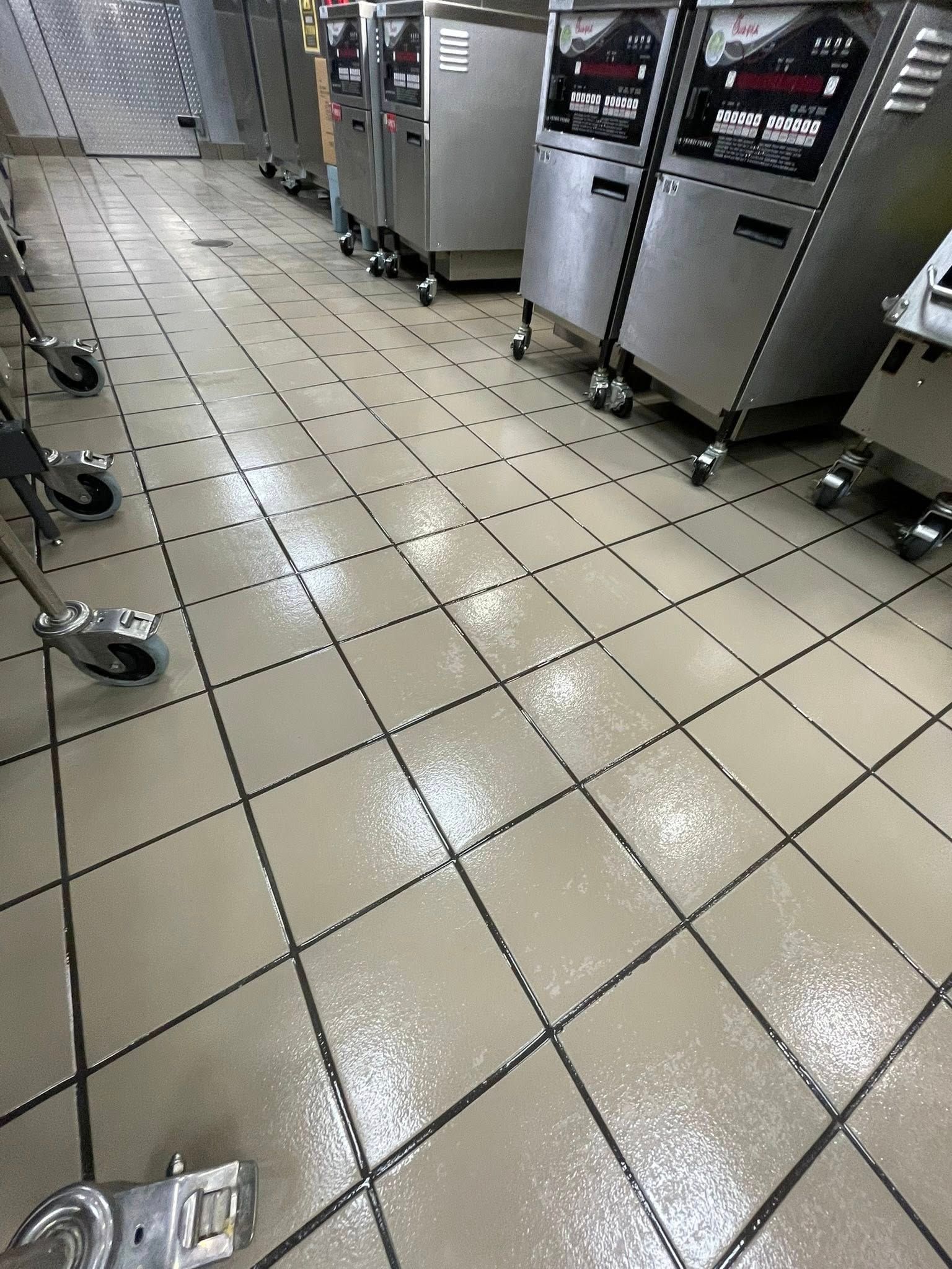 Shiny tiled floor in a commercial kitchen with stainless steel appliances and carts along the walls.