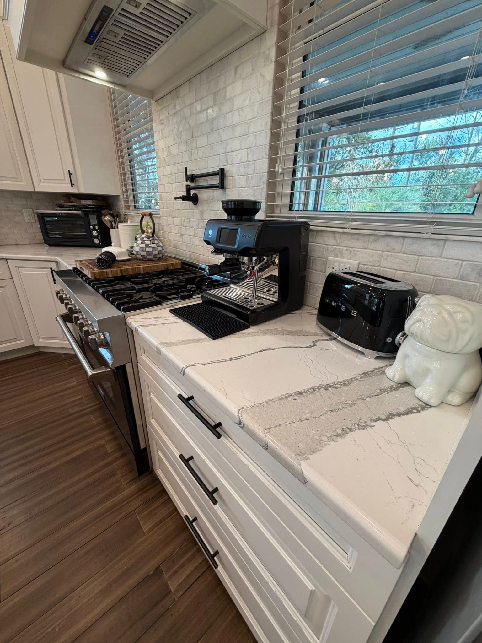 Modern kitchen with white cabinets, black countertops, stove, toaster oven, and coffee maker by a window