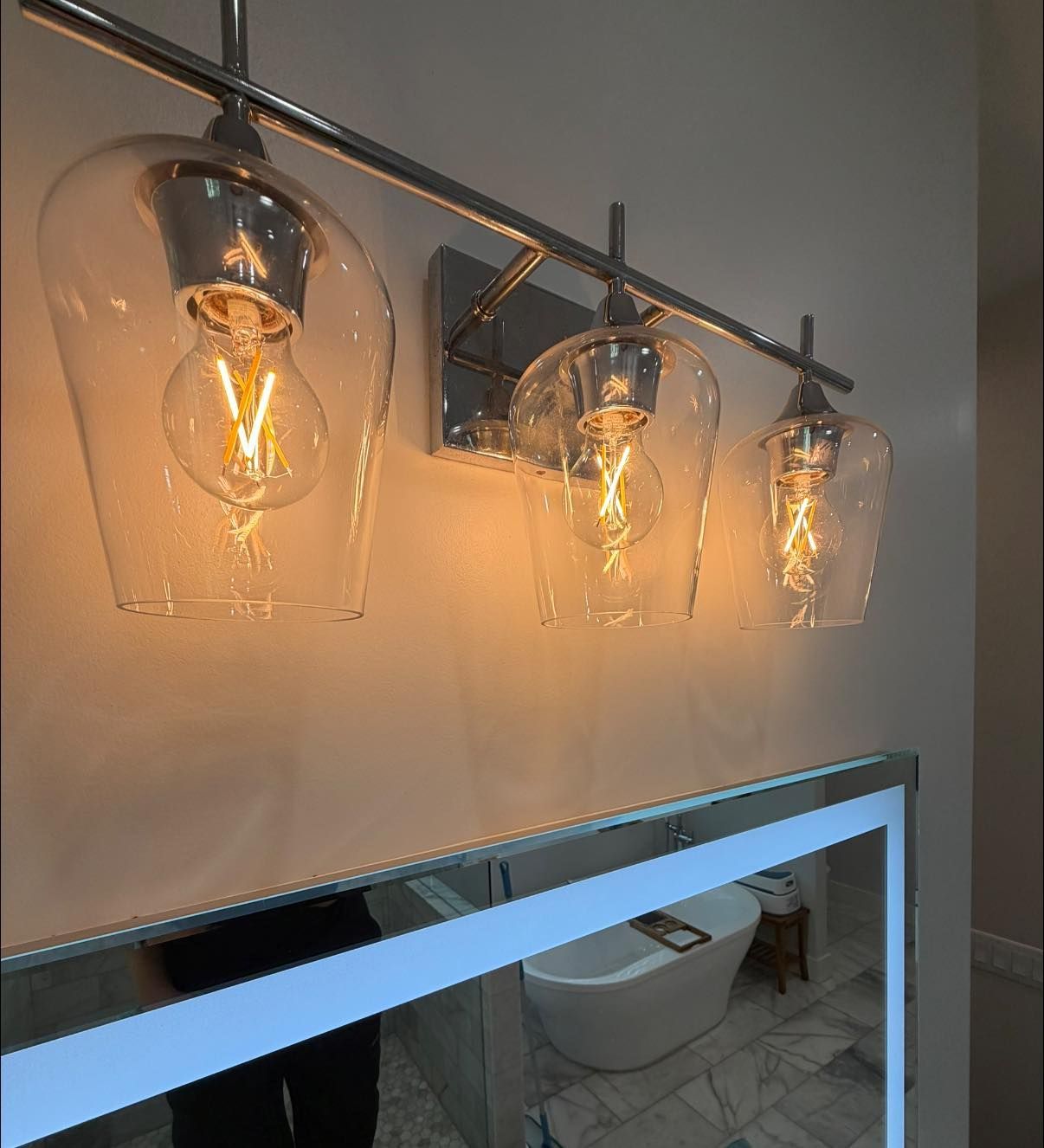 Three clear glass pendant lights above a bathroom mirror with a sink below
