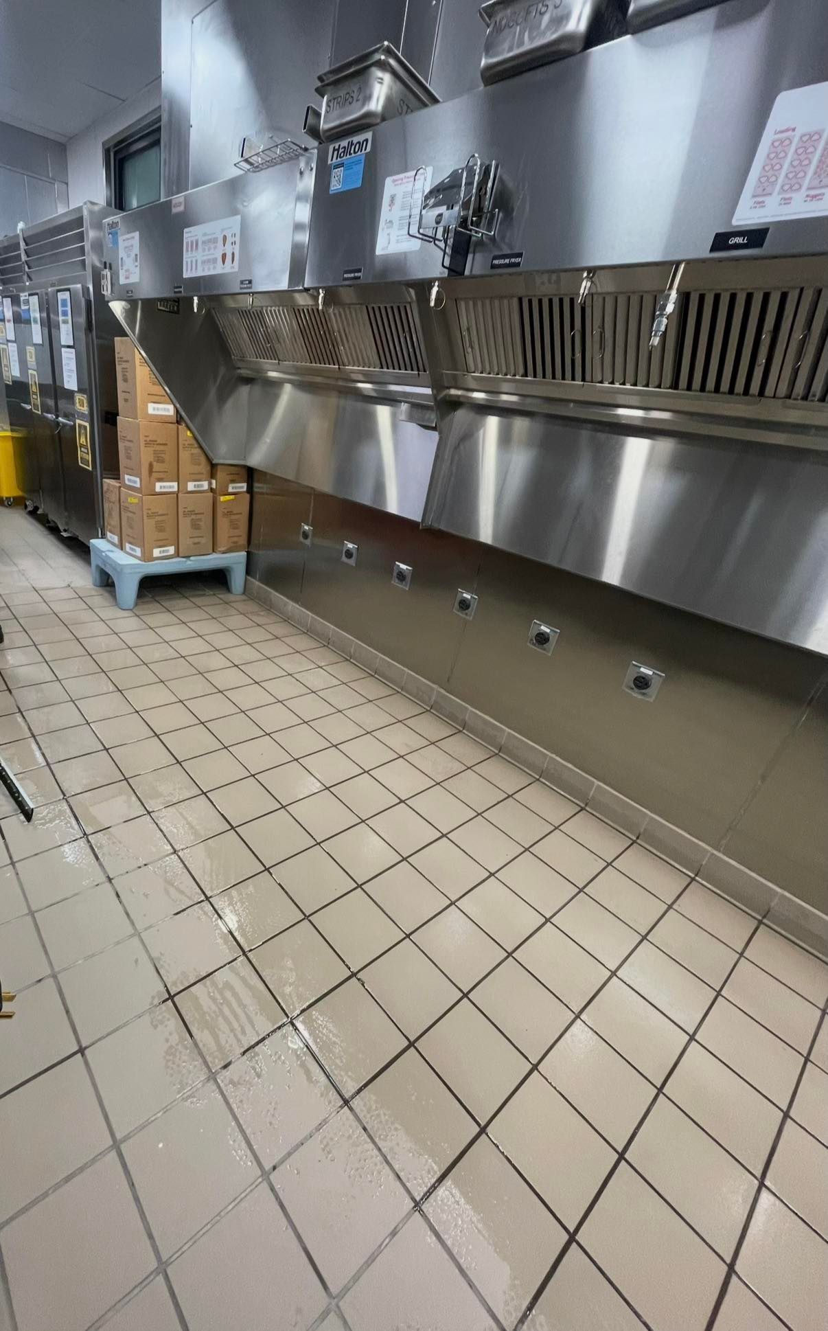Commercial kitchen with stainless steel counters, tiled floor, and stacked boxes on a cart