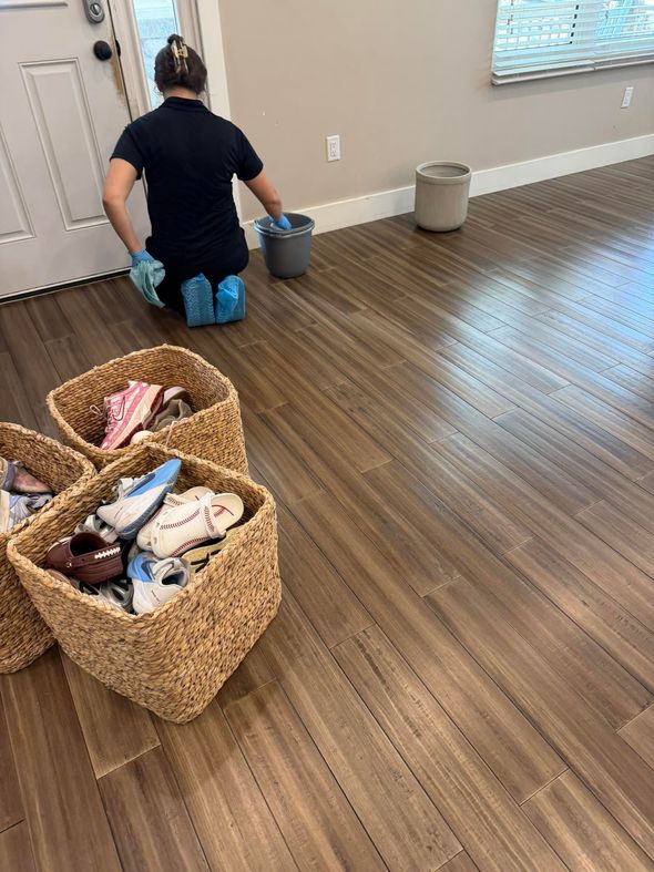Person mopping a hardwood floor in a room with woven laundry baskets nearby.