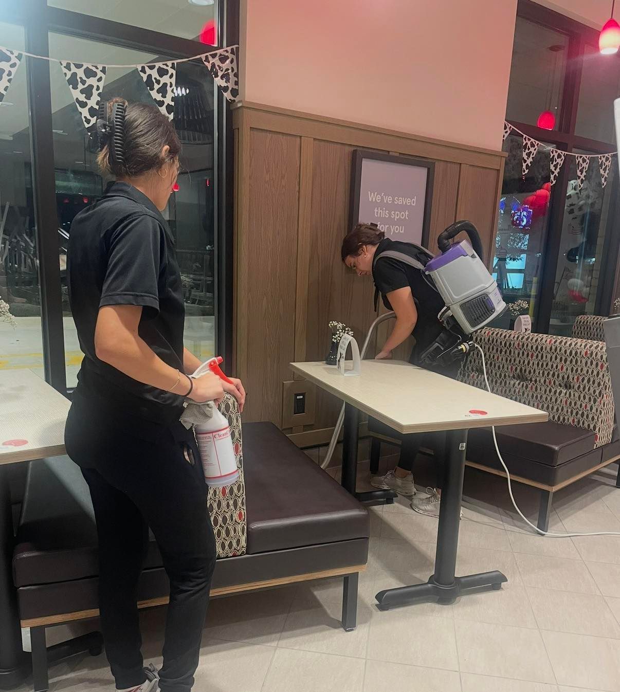 Person cleaning a tattoo booth with spray bottle and cloth in a salon interior