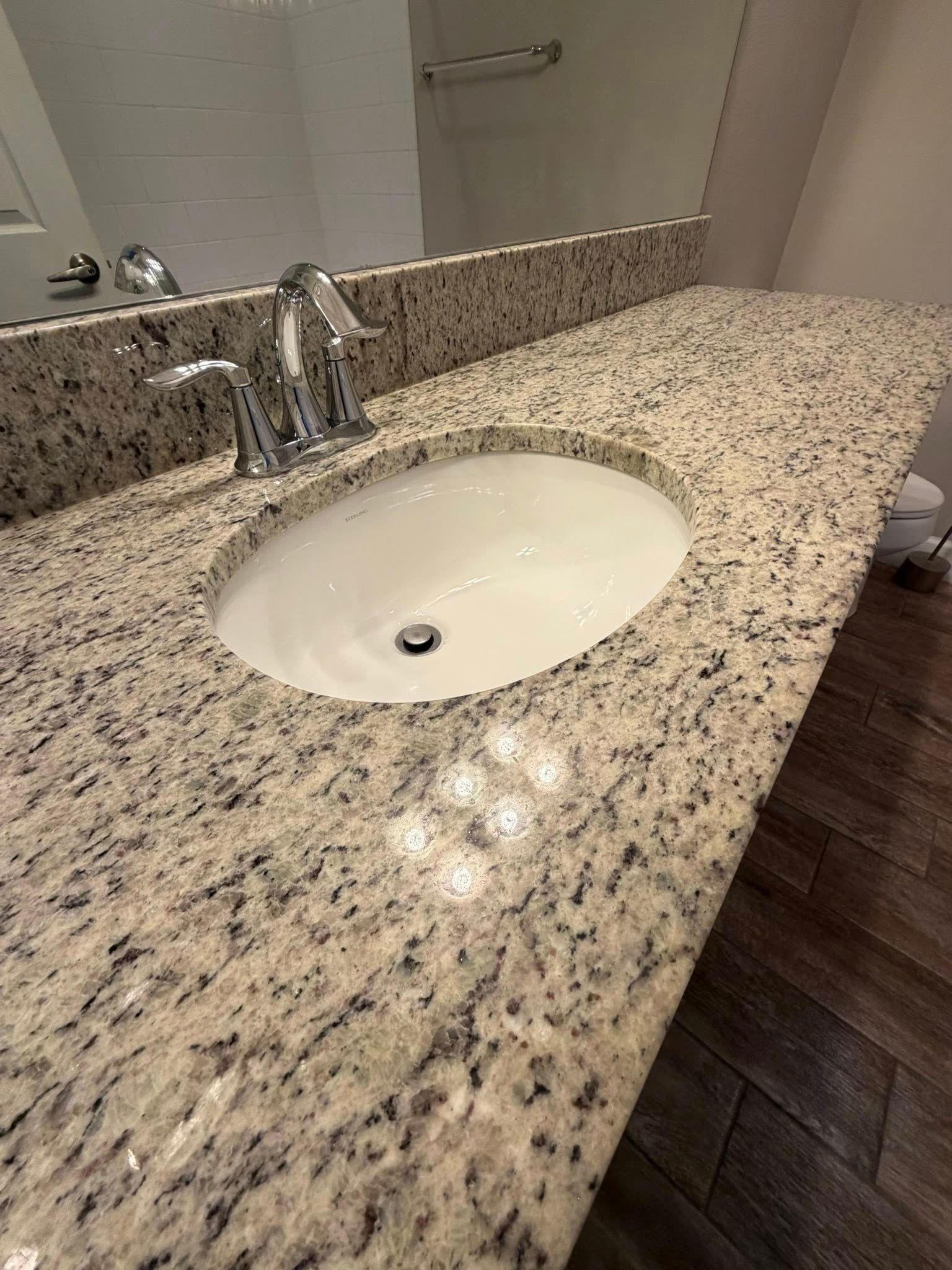 Bathroom vanity with speckled granite countertop, oval sink, and chrome faucet.