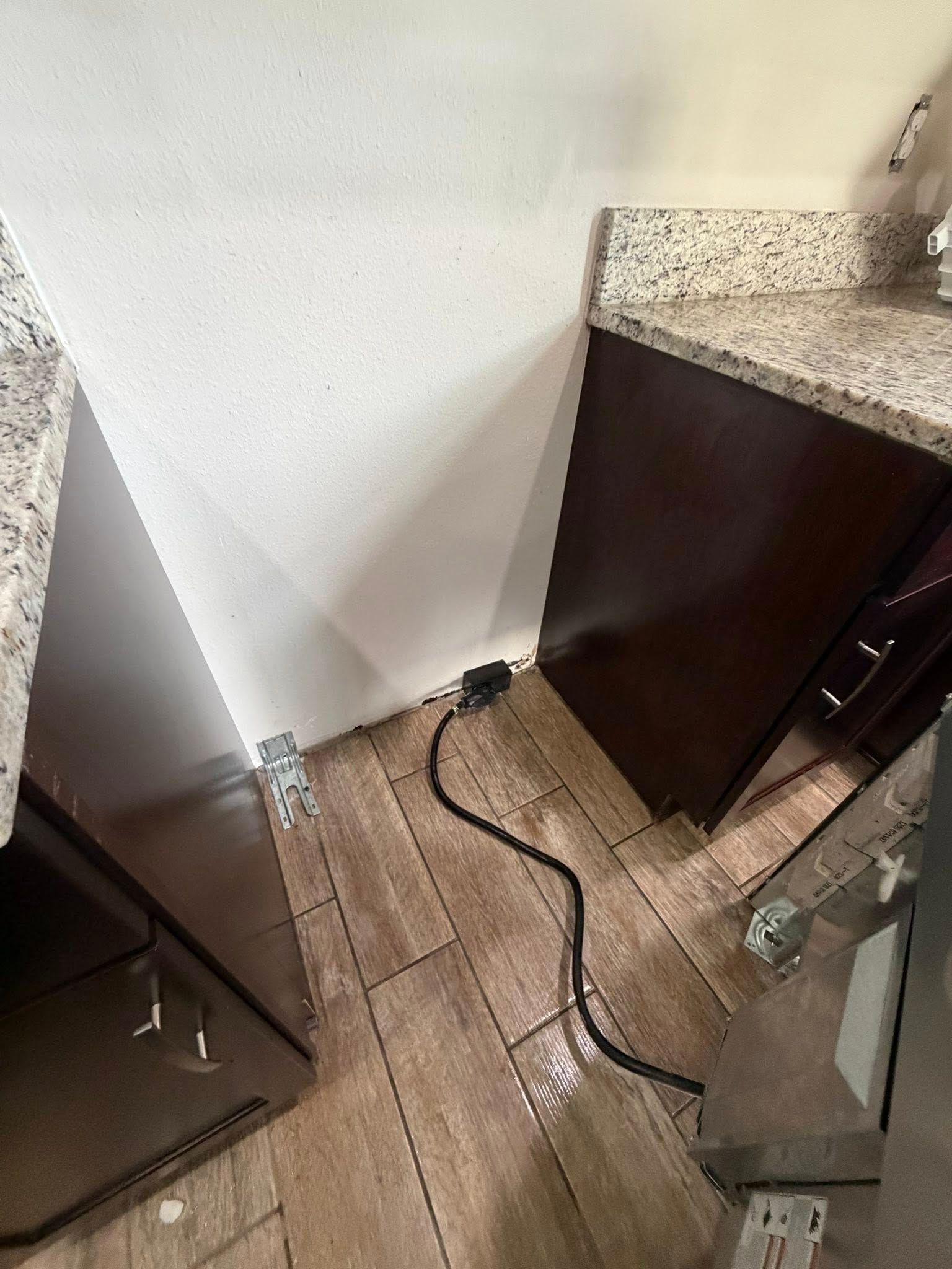 Kitchen floor with loose black cord between dark cabinets and a white wall near a speckled countertop