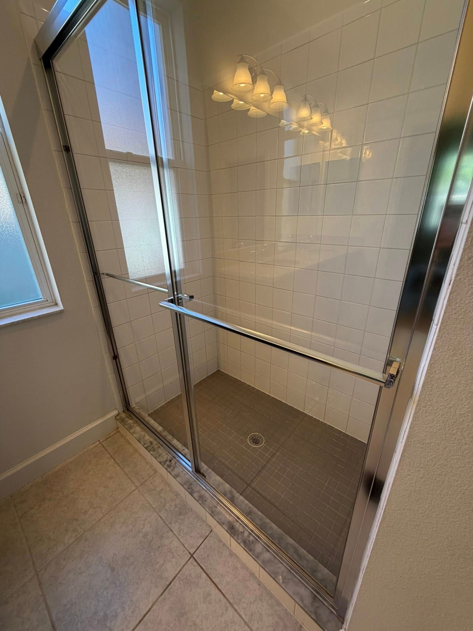 Glass walk-in shower with chrome sliding door and beige tile bathroom floor