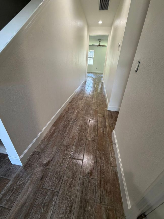 Narrow hallway with white walls and wood floor, leading to a bright window at the end.
