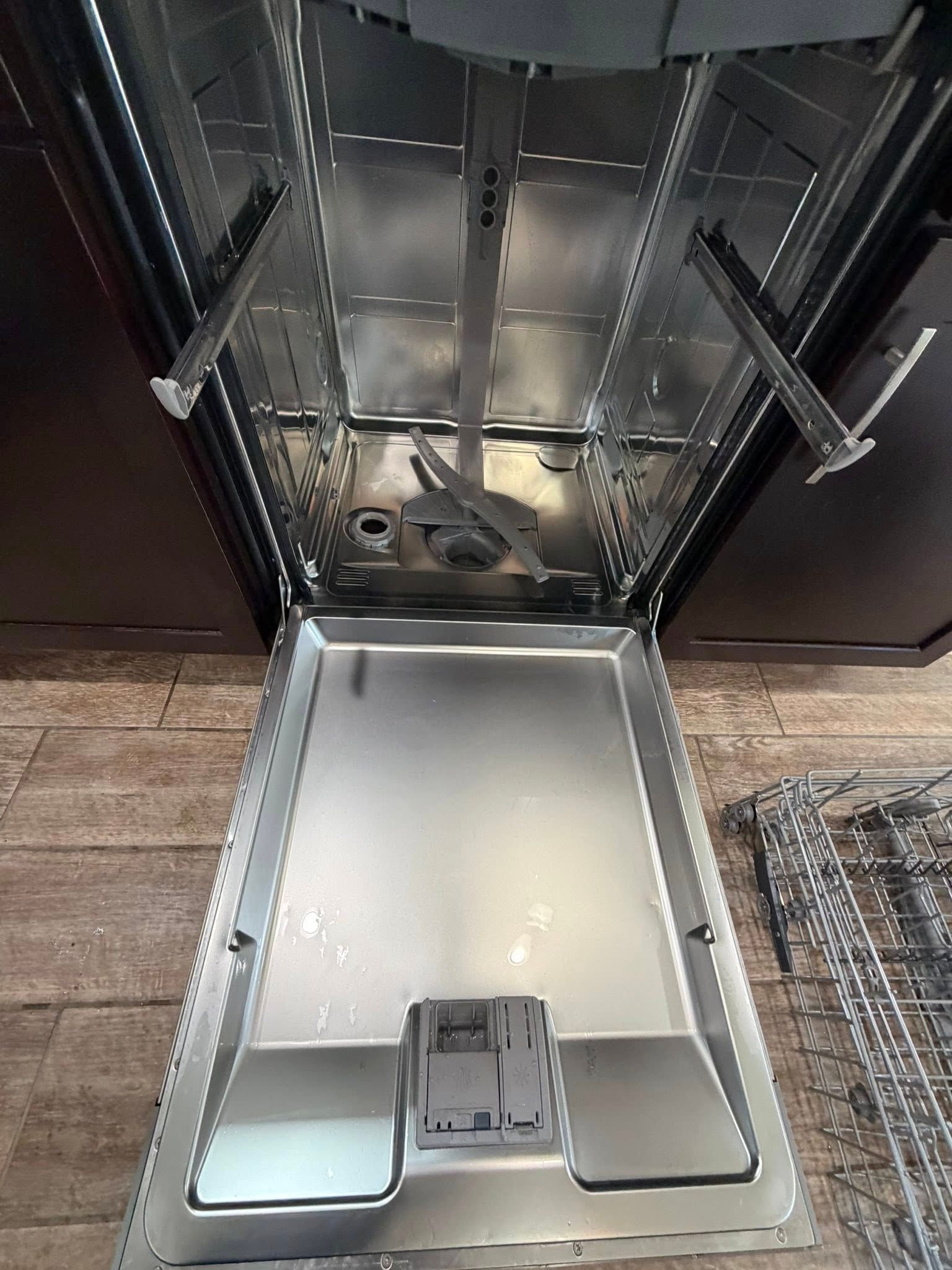 Open dishwasher with lower rack pulled out, showing empty stainless steel interior.