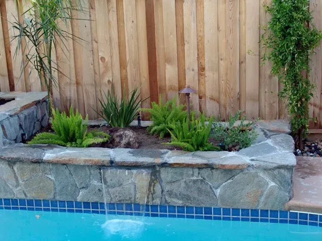 A swimming pool with a stone wall and a wooden fence surrounding it.