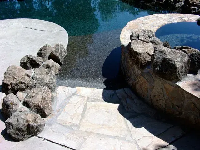 A stone patio next to a pool with rocks on it