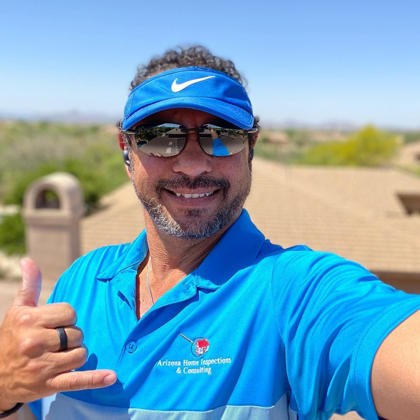 A man wearing sunglasses and a blue hat is giving a thumbs up.