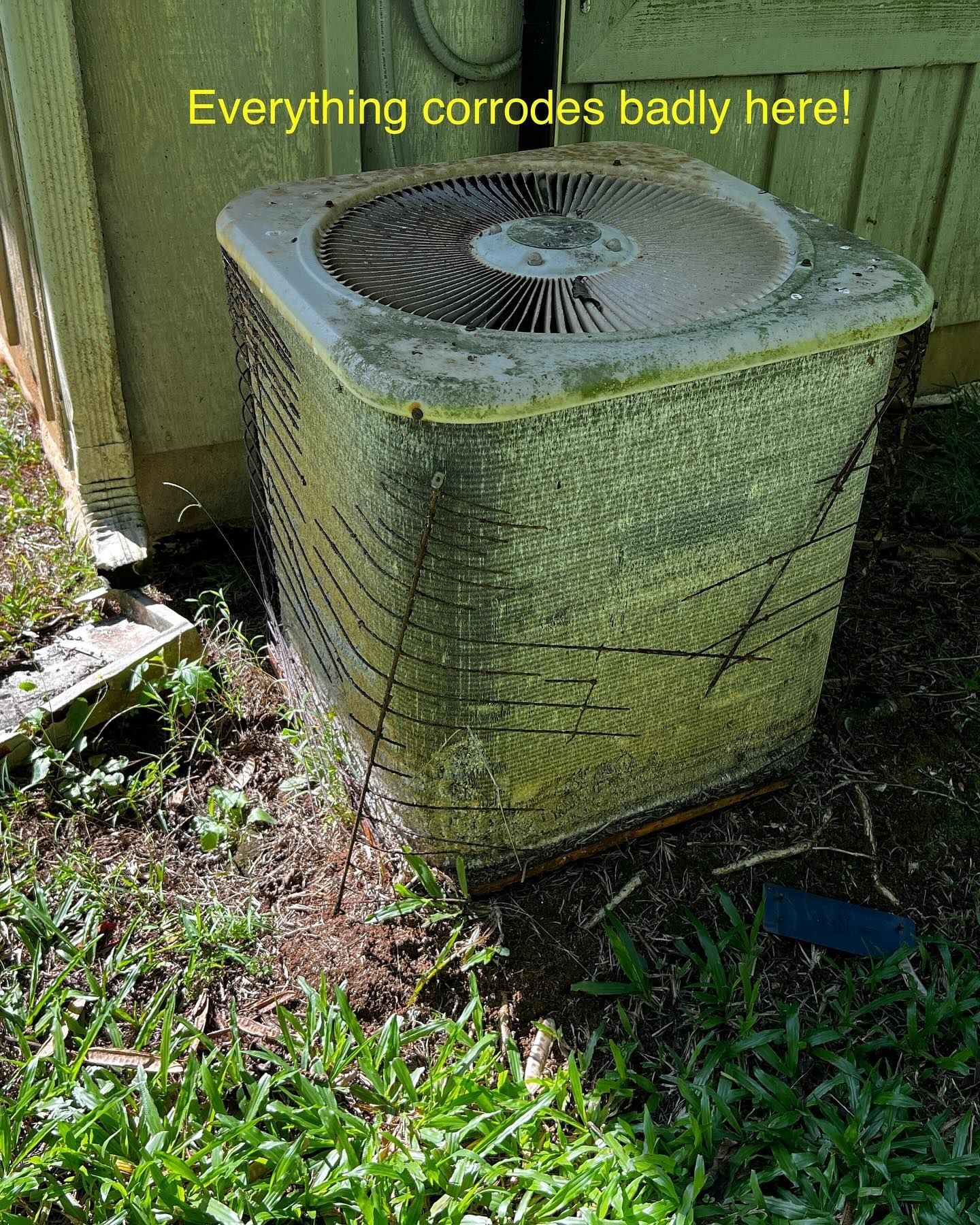 A dirty air conditioner is sitting in the grass next to a building.