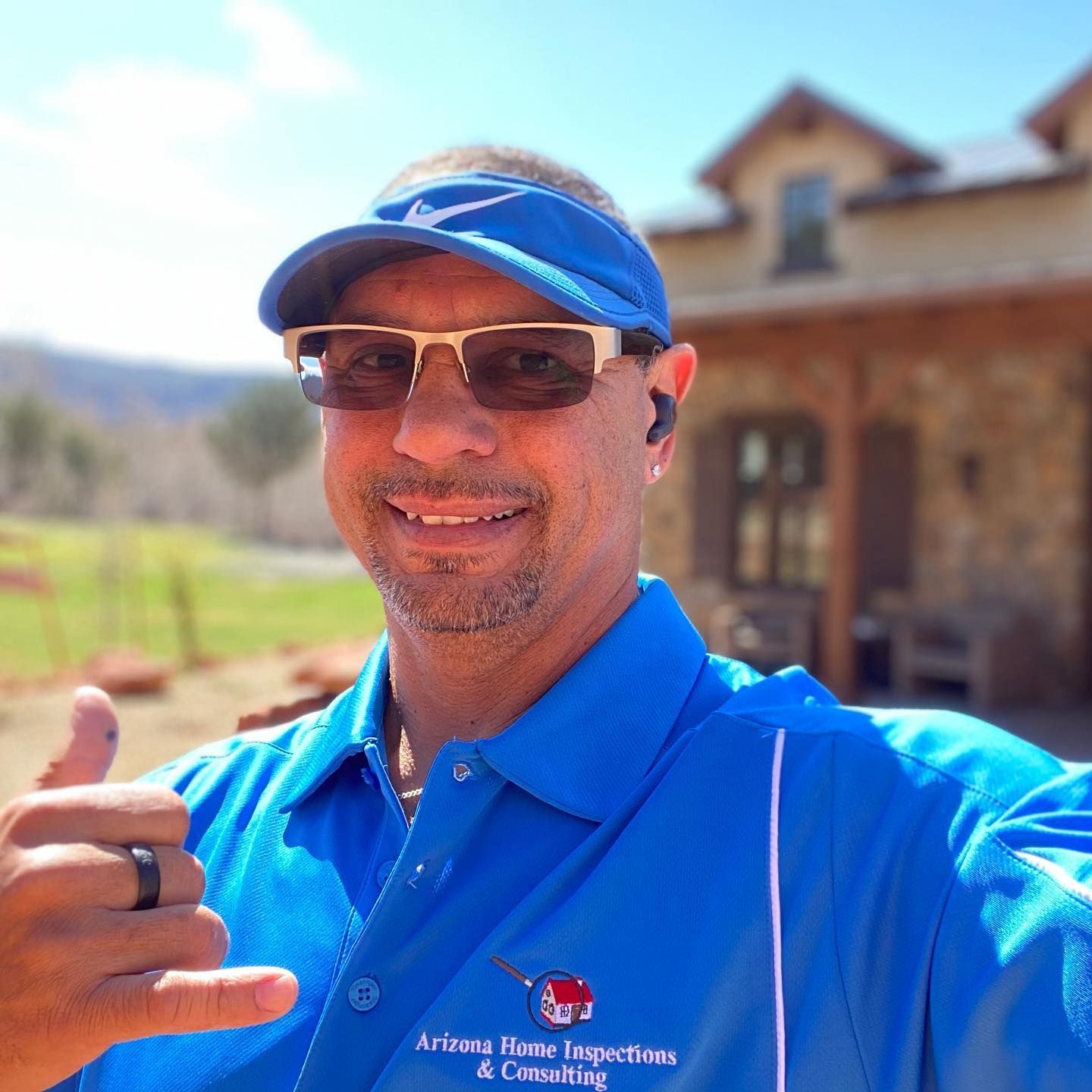 A man wearing sunglasses and a blue shirt is giving a thumbs up