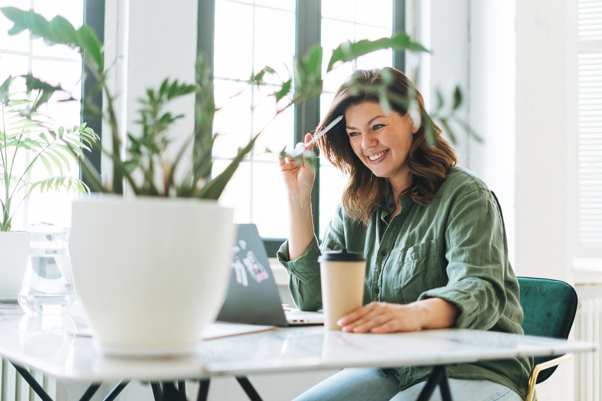 A woman is sitting at a desk with a laptop and a cup of coffee.