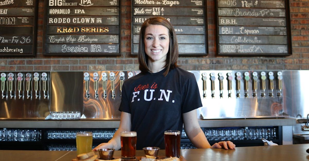 A woman wearing a black shirt that says fun is standing at a bar.