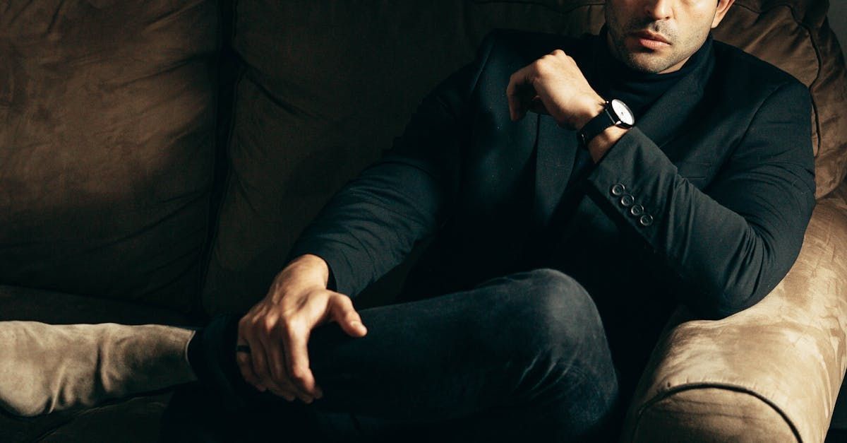 A man in a suit is sitting on a couch wearing a watch.