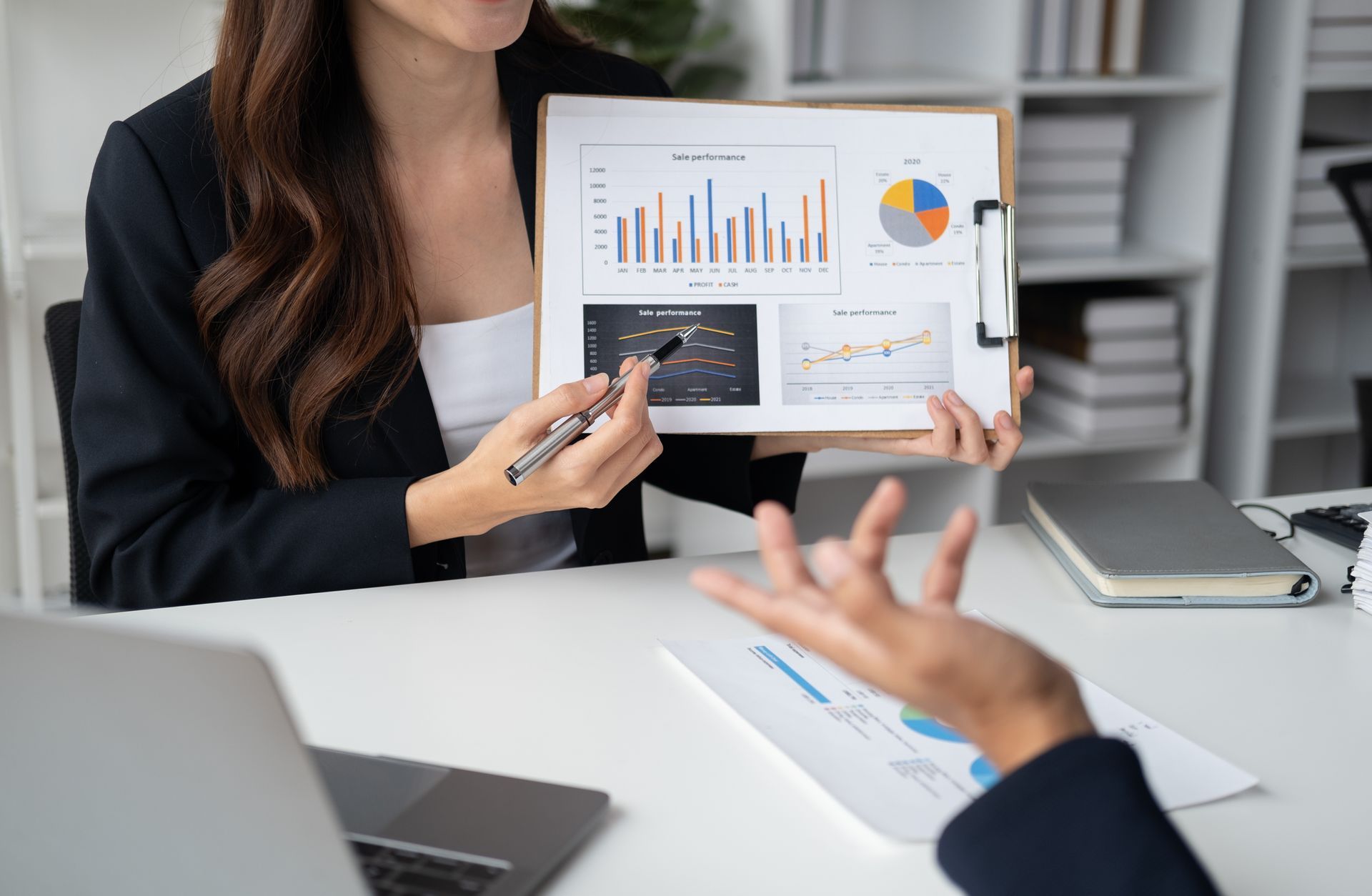 A woman is holding a clipboard with graphs on it and talking to a man.