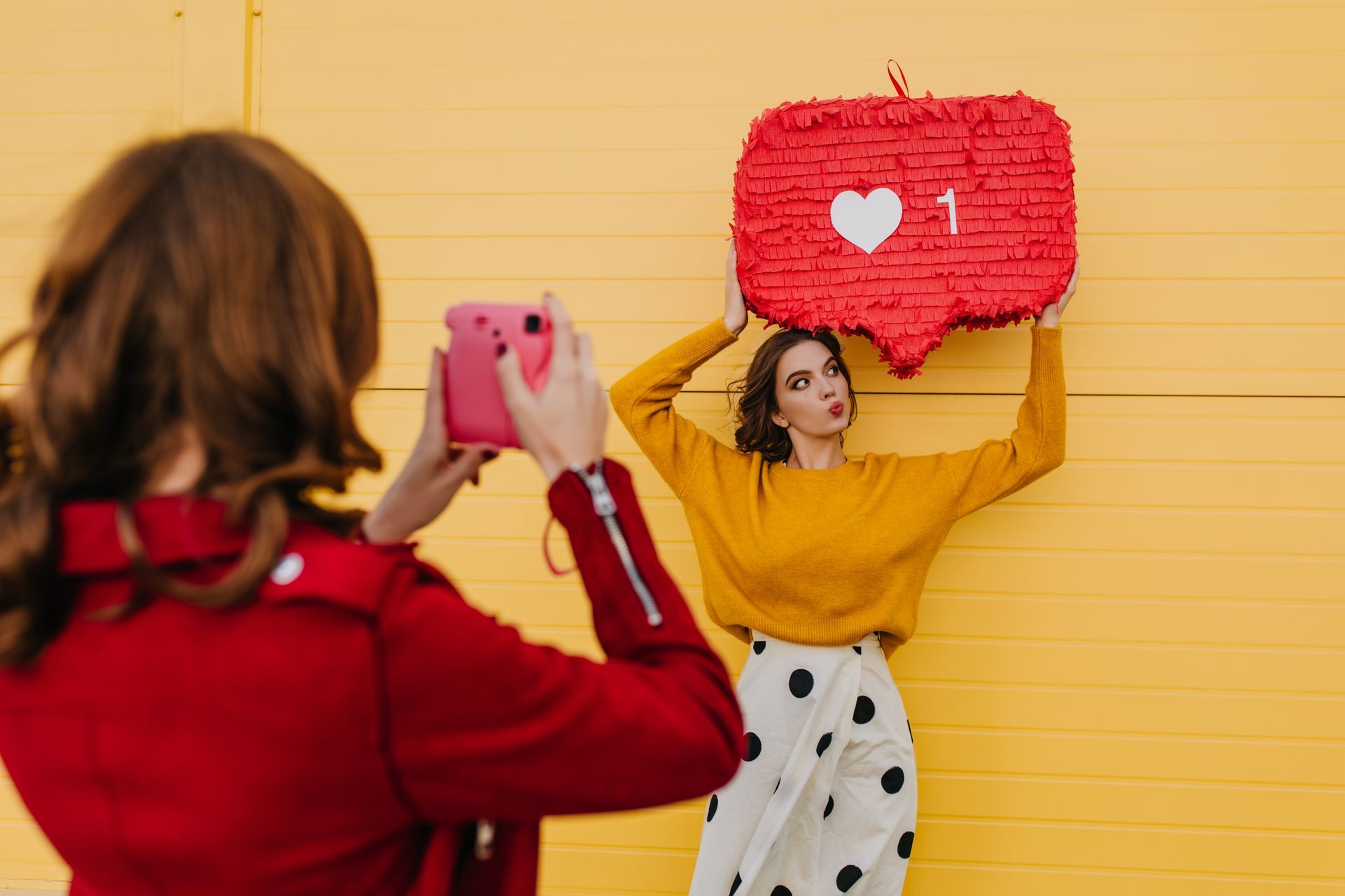 A woman is taking a picture of another woman holding a piñata.
