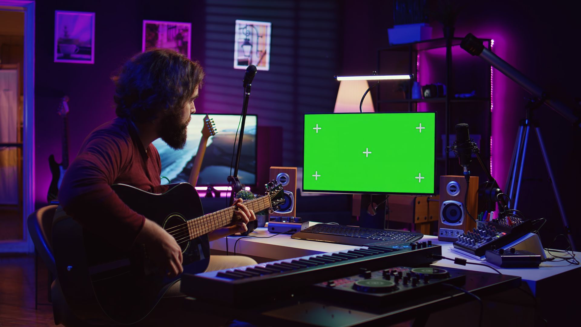 A man is playing a guitar in front of a green screen in a recording studio.