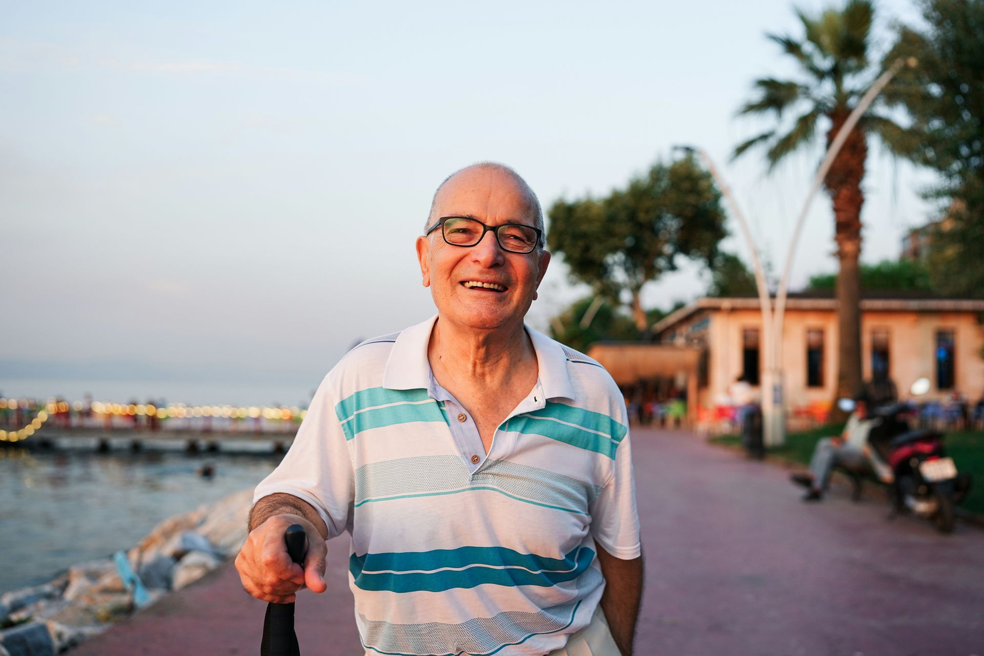 An elderly man is standing on a sidewalk holding a cane.