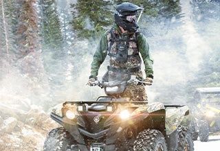 Person on an ATV in a snowy forest, wearing a helmet and camouflage clothing. | Impact Automotive