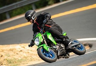 Green motorcycle leaned over in a curve on a winding road. Rider in black gear and helmet. | Impact Automotive