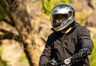 Person wearing a silver motorcycle helmet and black jacket, holding handlebars outdoors. | Impact Automotive