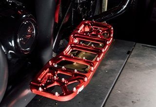 Red motorcycle footrest, metal, with sharp points and cut-out sections. | Impact Automotive