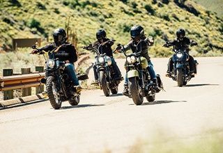 Four people ride motorcycles on a winding road with mountainous scenery. | Impact Automotive