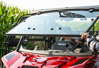 Red UTV with windshield being installed outdoors, person holding a wiper blade. | Impact Automotive