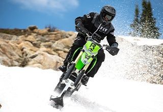 Snow biker in action on a snowy slope. Green and black motorcycle, blue sky. | Impact Automotive