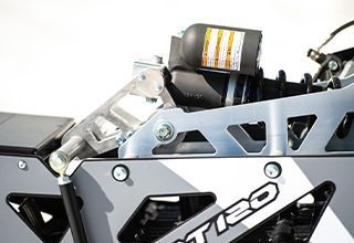 Close-up of a snowmobile suspension system, featuring silver metal components and a black shock absorber against a gray patterned base. | Impact Automotive