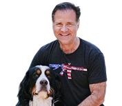 Man with a smiling expression sits next to a dog; man wears a shirt with a gun design. | Impact Automotive