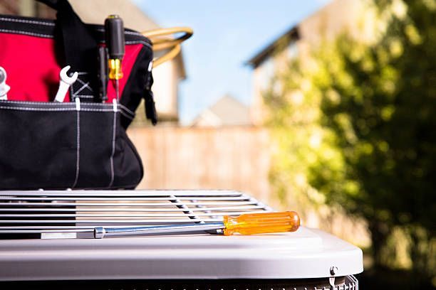 Tool bag with tools on an air conditioning unit in a backyard.