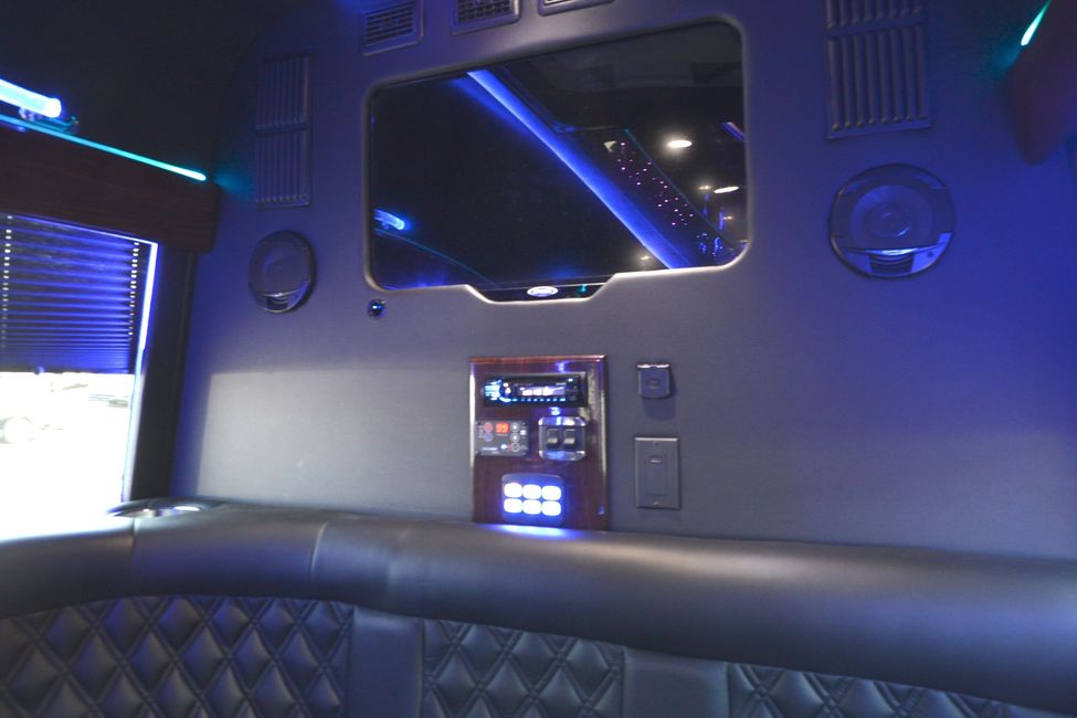 Interior of a limo with a TV, control panel, speakers, and blue lighting. Black leather seating.