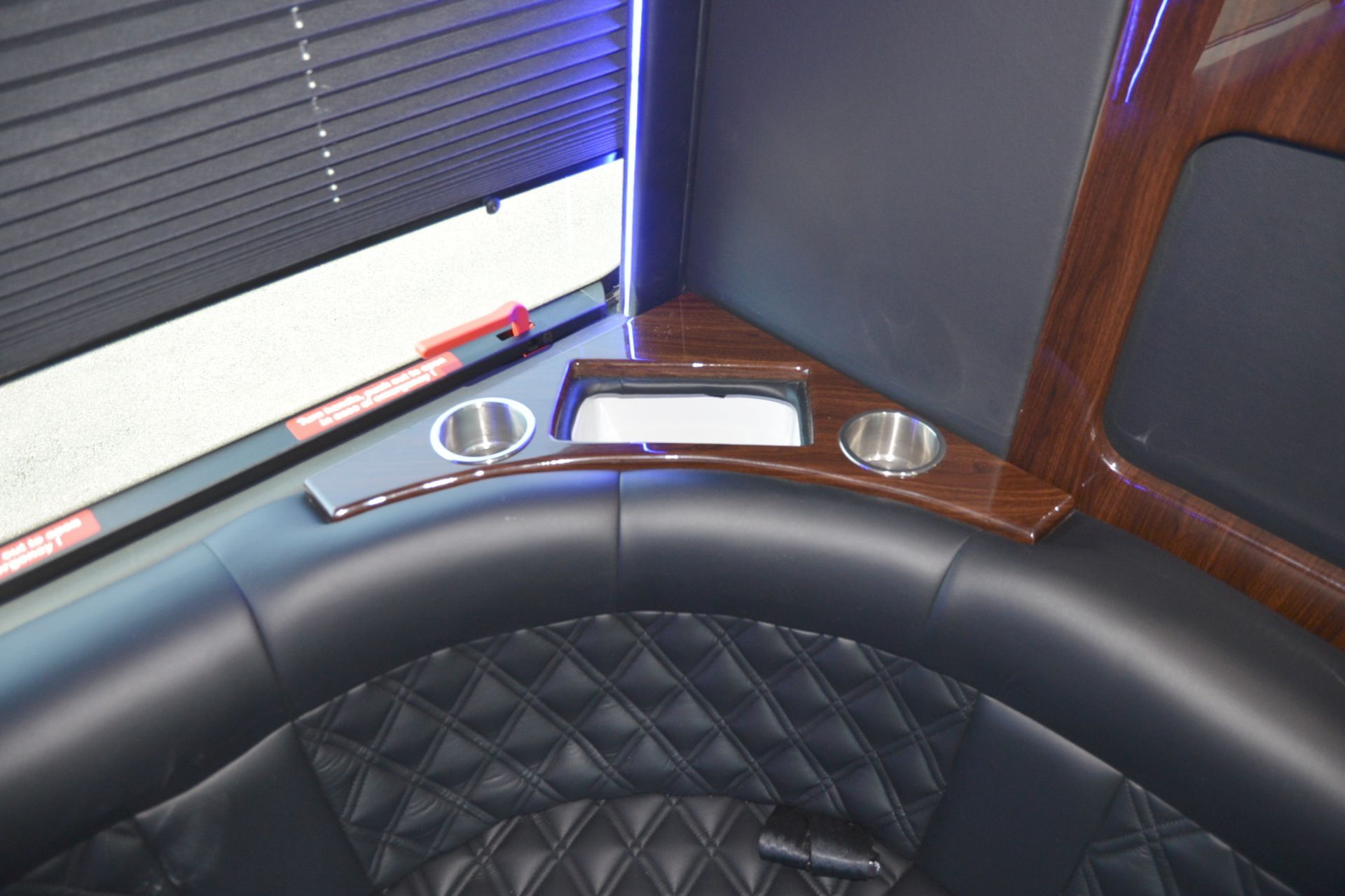 Interior of a luxury vehicle. Black leather seating with diamond stitching, wood trim, and cup holders.