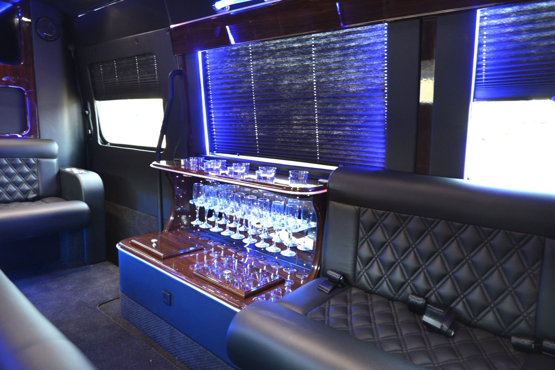 Interior of a luxury party bus with black leather seating, a bar, and blue lighting.