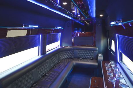 Interior of a luxury van with diamond-stitched black leather seating, blue neon lights, and a bar area.