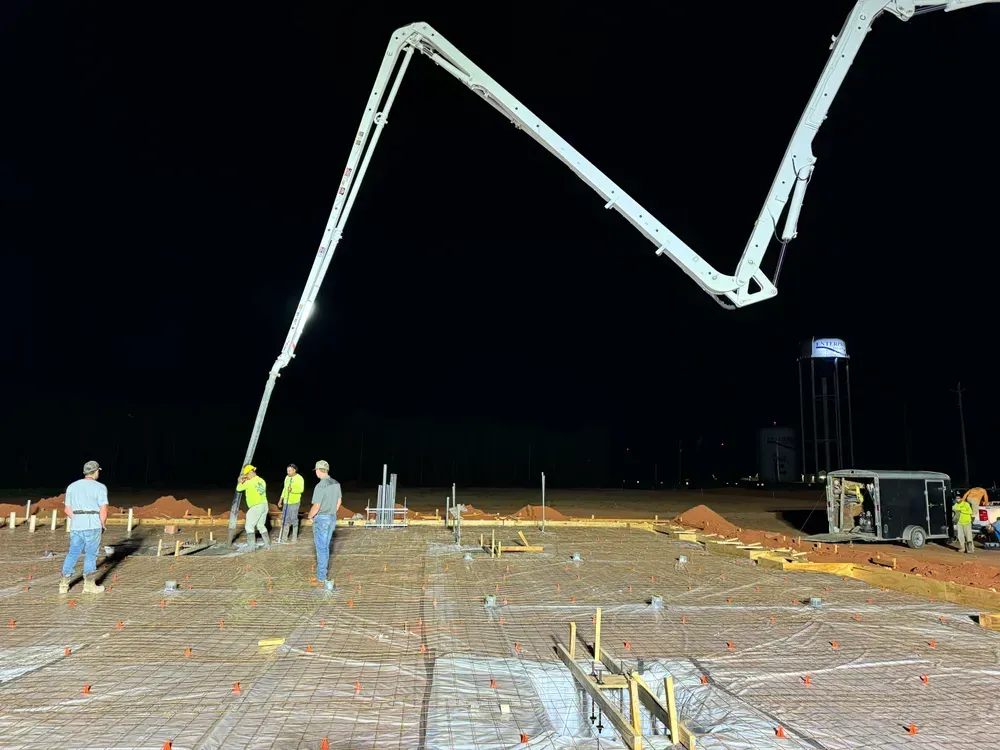 A concrete pump is being used to pour concrete on a construction site at night.