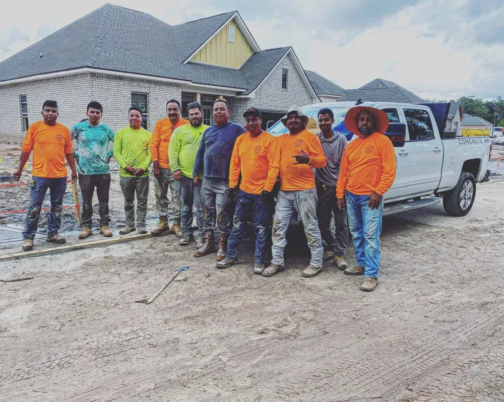 A group of construction workers are posing for a picture in front of a house under construction.
