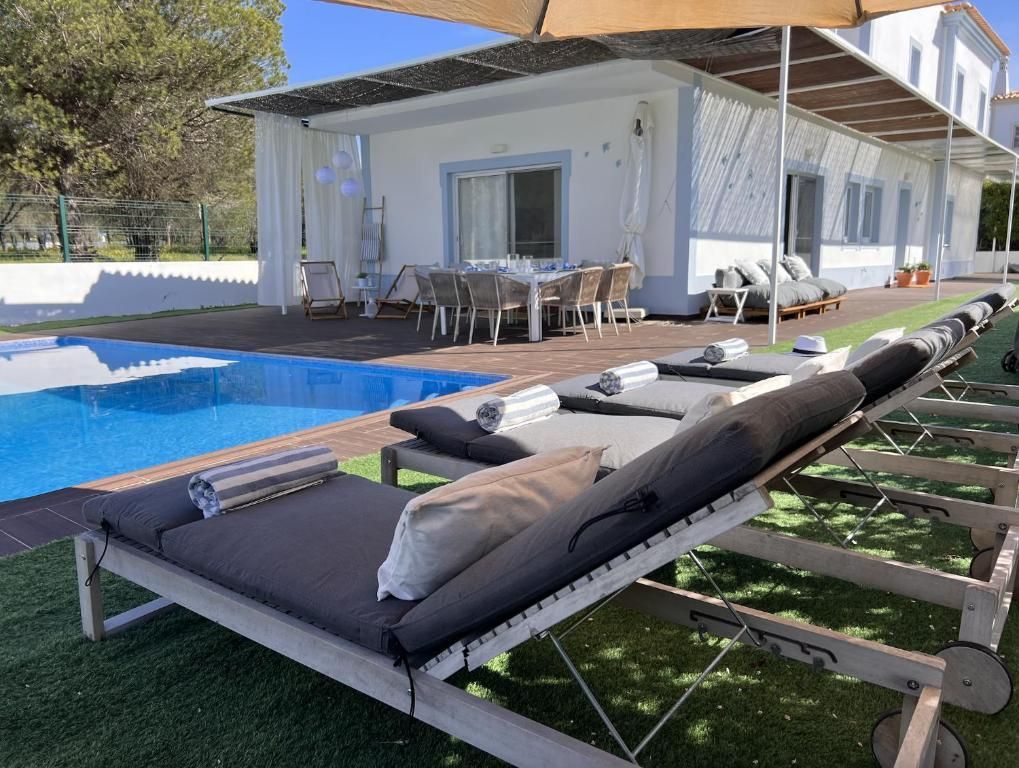 A row of lounge chairs is next to a pool in front of a house.