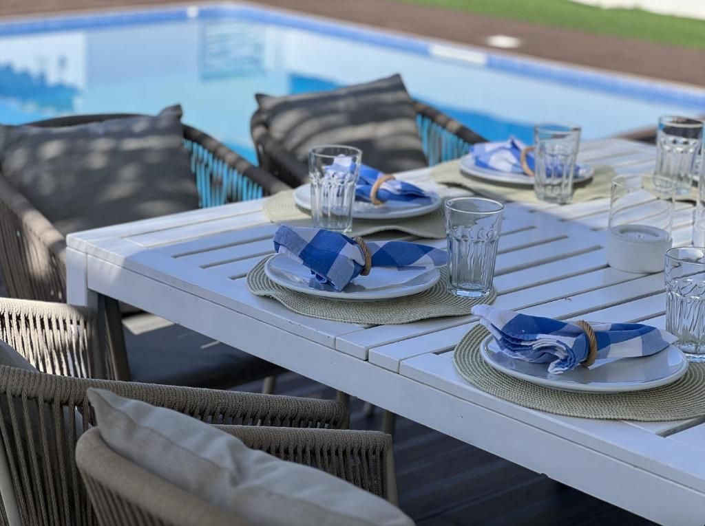 A table with plates, glasses and napkins is next to a pool.