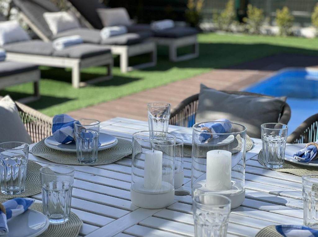 A table with plates, glasses and candles prepared for a meal in front of a swimming pool.