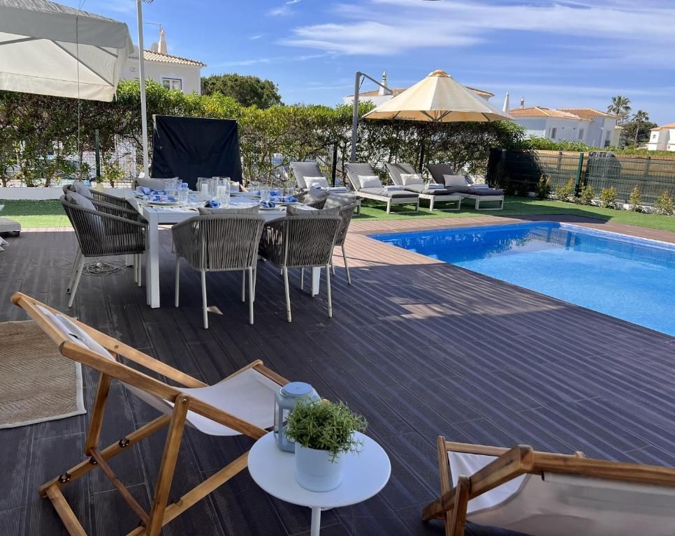 A large pool is surrounded by a wooden deck with chairs and tables.