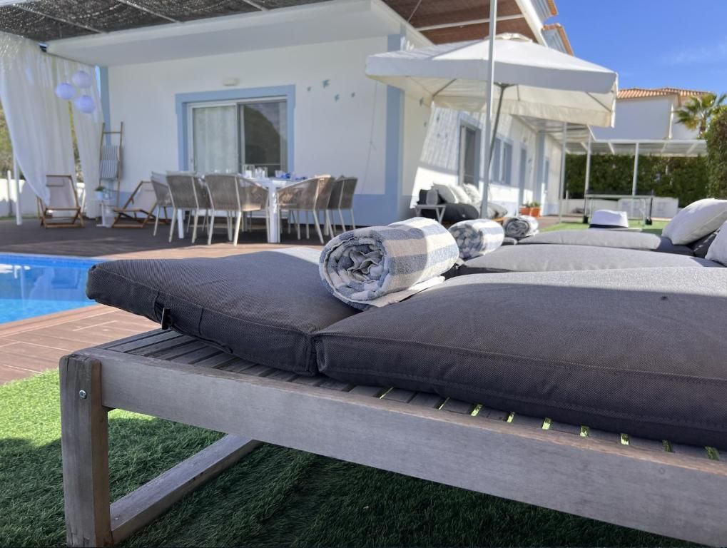 A row of lounge chairs is next to a pool in front of a house.