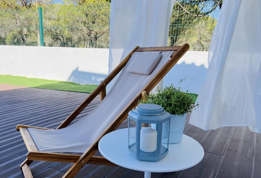 A wooden lounge chair sits on a wooden deck next to a white table.