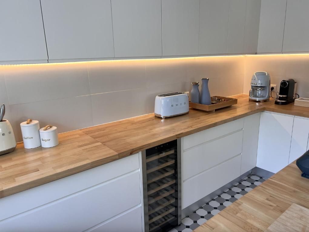 A kitchen with white cabinets, wooden countertops and a wine refrigerator.