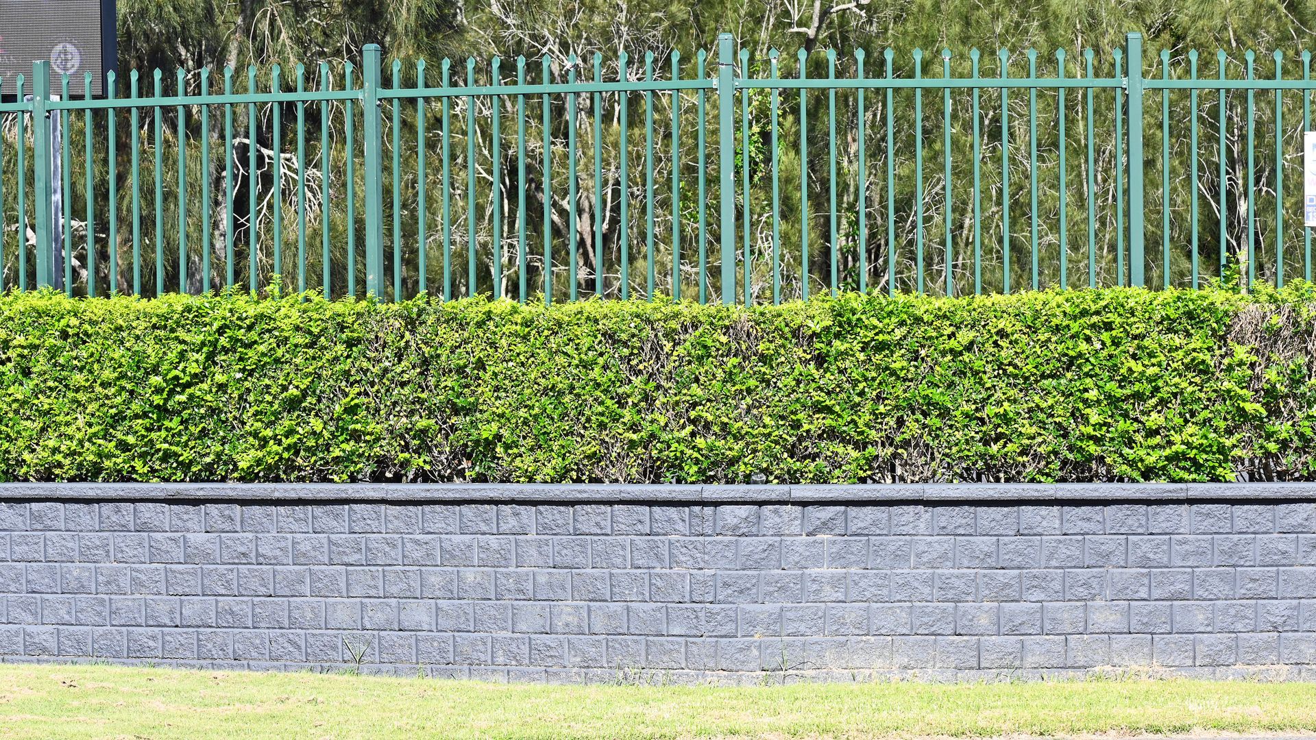 Concrete block retaining wall with metal fence and lush garden hedge. Concrete block retaining wall with metal fence and lush garden hedge.