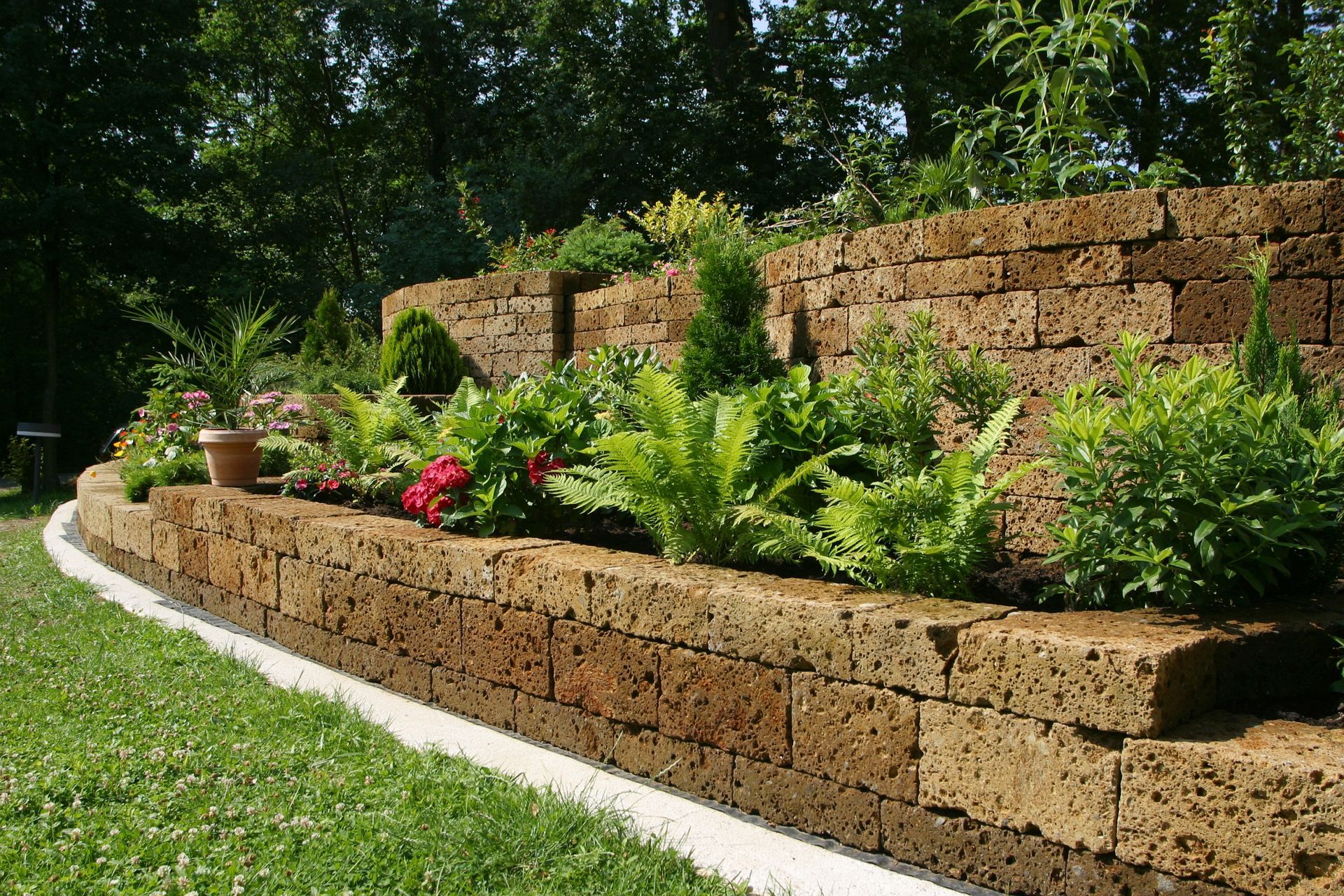 Tiered stone garden wall with green plants and flowers.